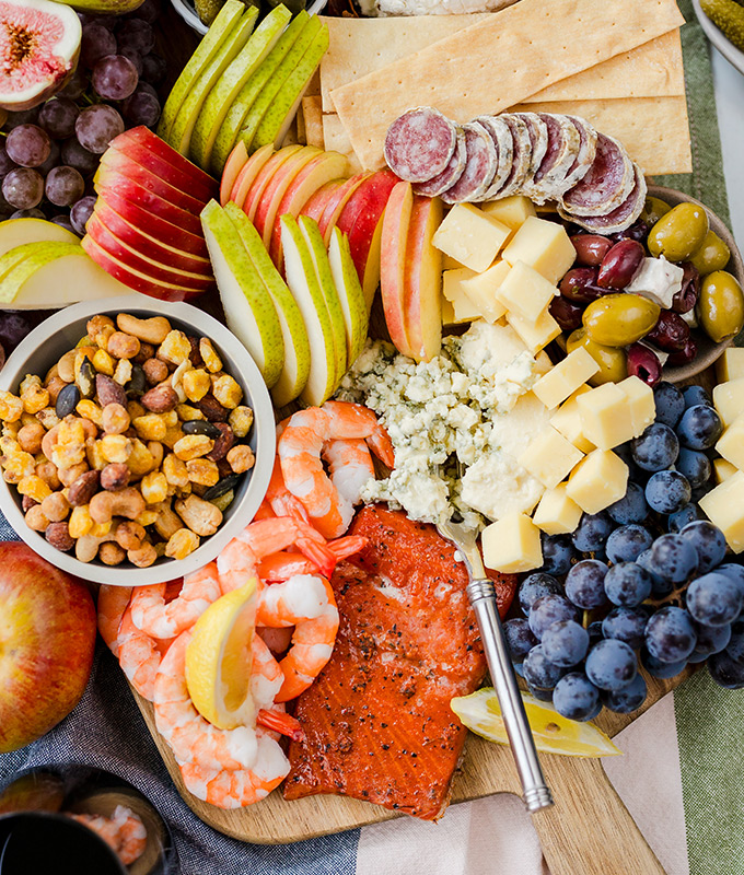 A bountiful board of sliced meat and cheese with fruit and nuts.