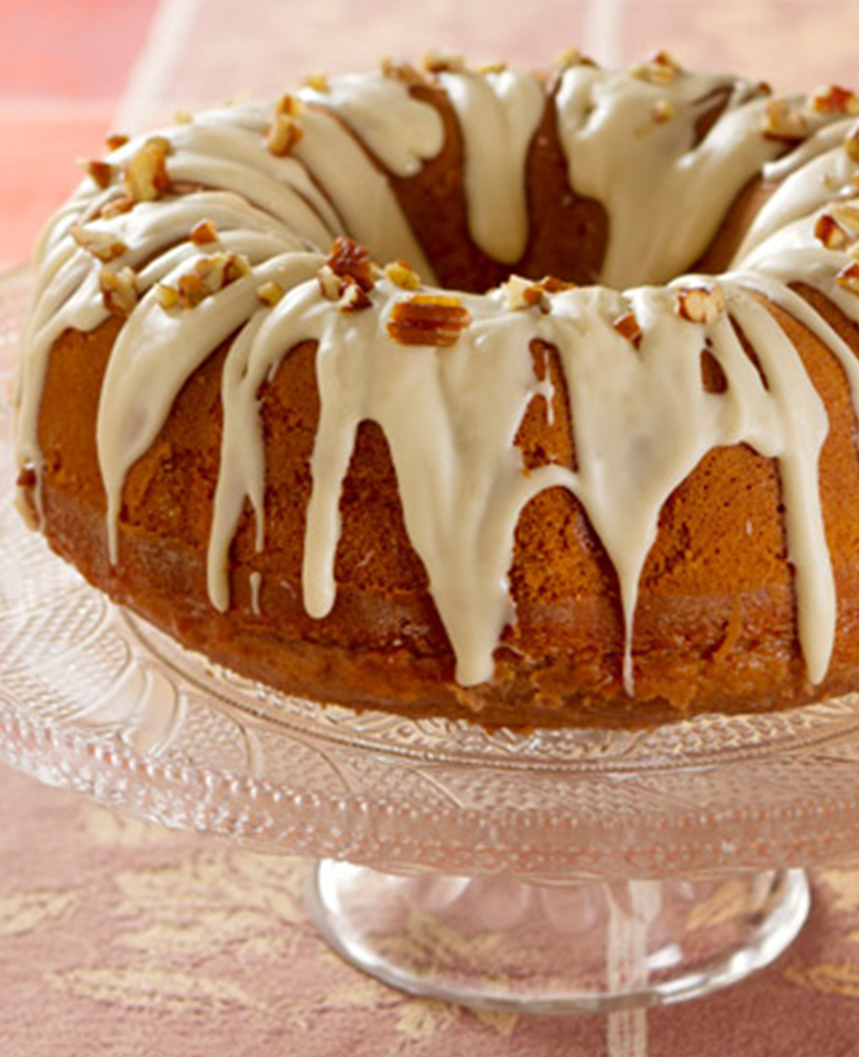 An apple pecan bundt cake with a white powdered-sugar glaze and chopped pecans. 