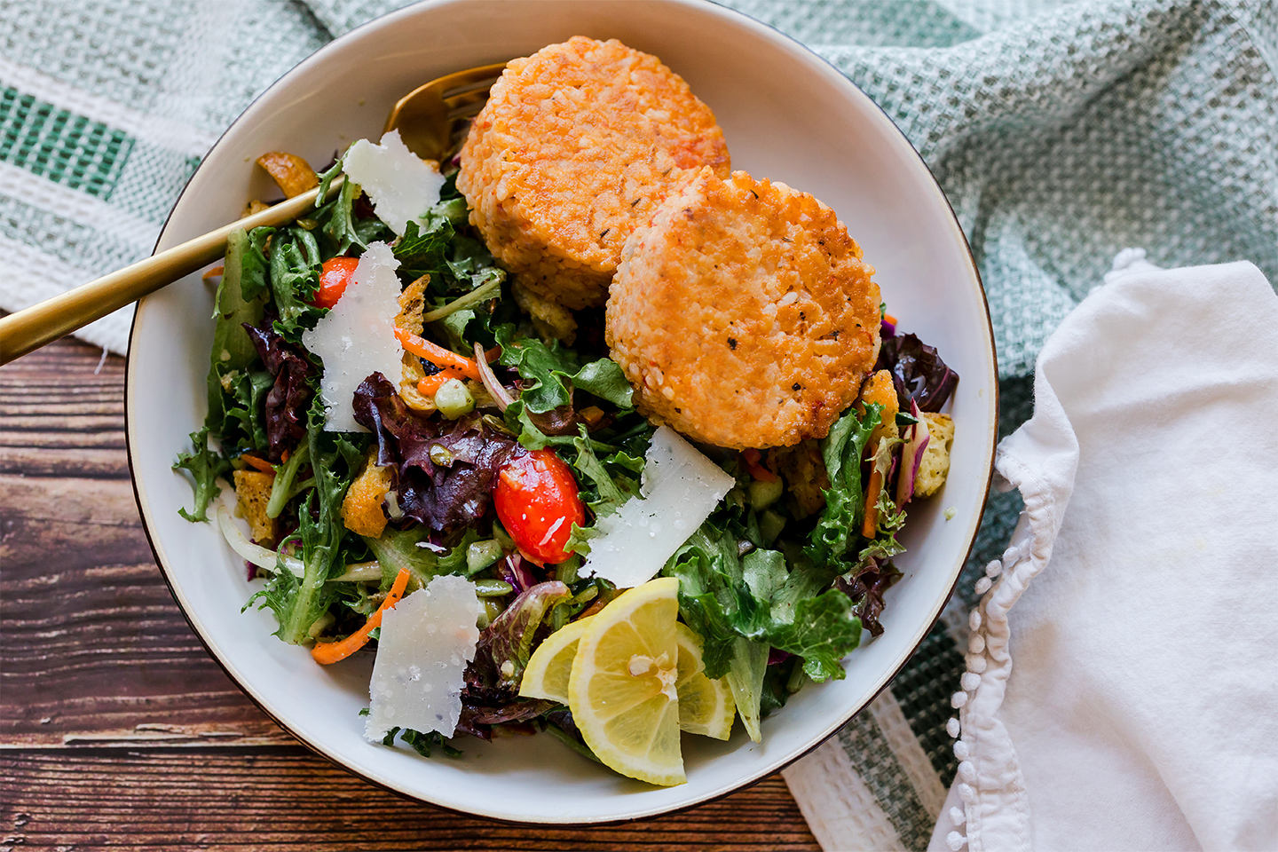 a bowl of fresh salad with risotto cakes on top.