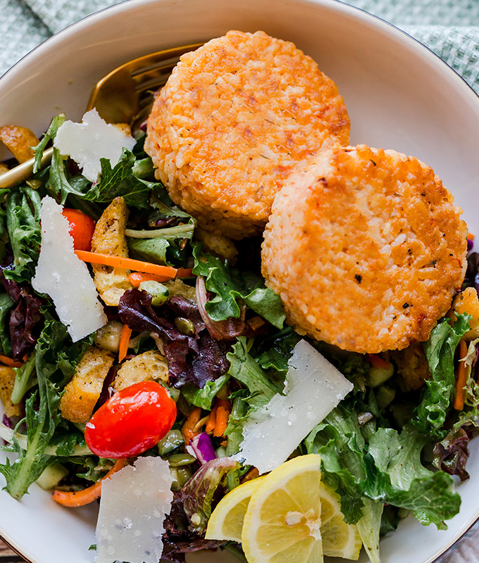 A fresh salad with vegetables and two risotto cakes.
